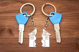 Two house keys with blue tops and matching metal keychains shaped like a broken house, lying on a wooden surface — symbolizing divided property ownership or a real estate dispute between co-owners. where a partition might make sense.